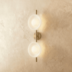 Clérachic two-shade wall light with frosted white glass dishes glowing soft on a brushed gold vertical rod and round backplate.