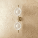 Clérachic two-shade wall light with white glass dishes and opal globes on a brushed gold rod, switched off on plaster.
