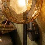 Close-up of a Clérachic amber rippled glass shade with a frosted bulb on a black rod and round backplate, glowing warm.