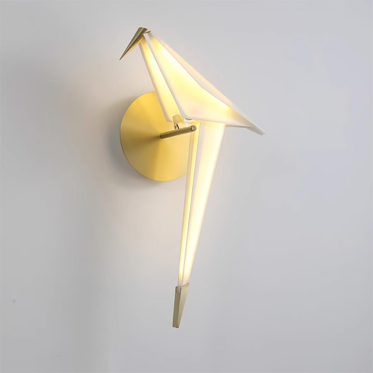 A lit Clérachic bird wall light on a pale grey wall, its folded white body glowing along the tail above a round gold backplate.