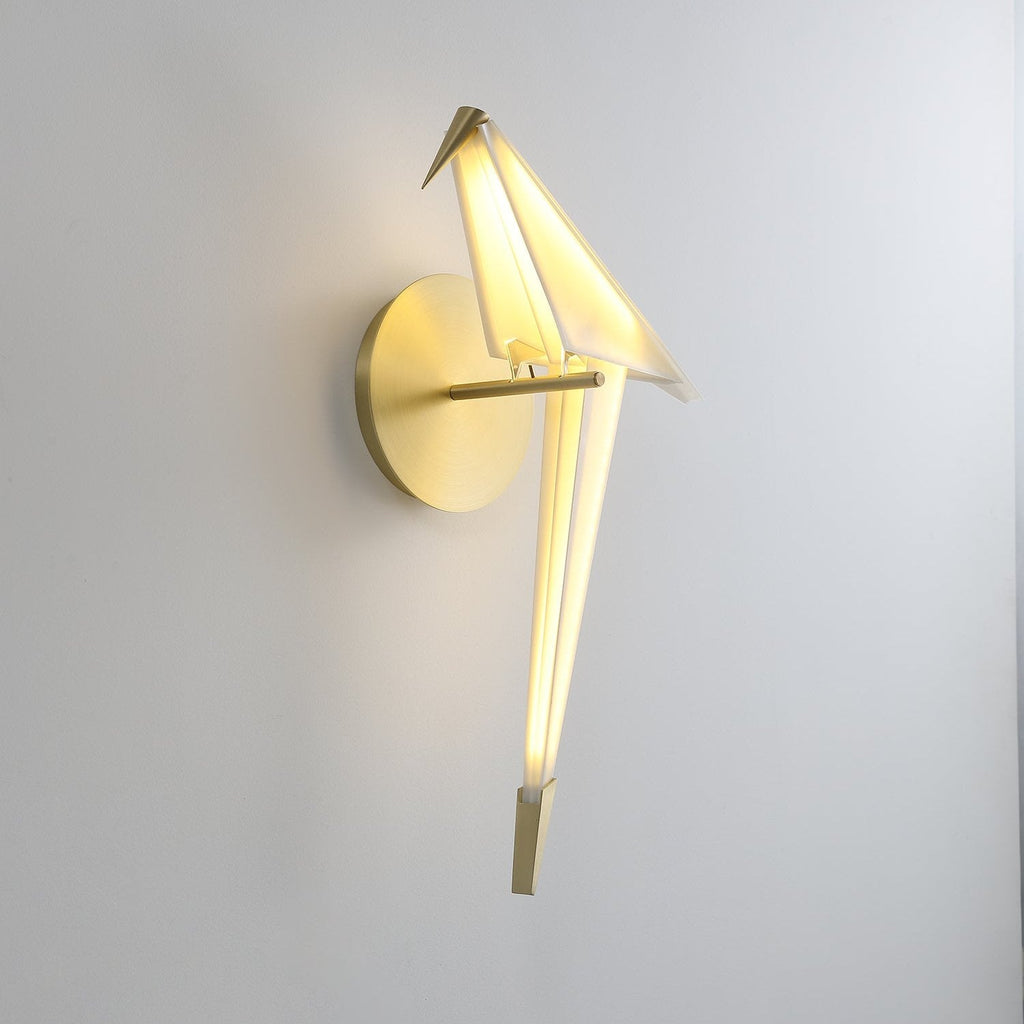 Seen from a slightly raised angle, this Clérachic bird wall light glows warm from its folded white body, with a gold tip on the tail.