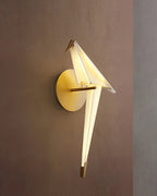 Against a dusty rose wall, this Clérachic bird wall light shows a lit white body and a gold backplate and perch.
