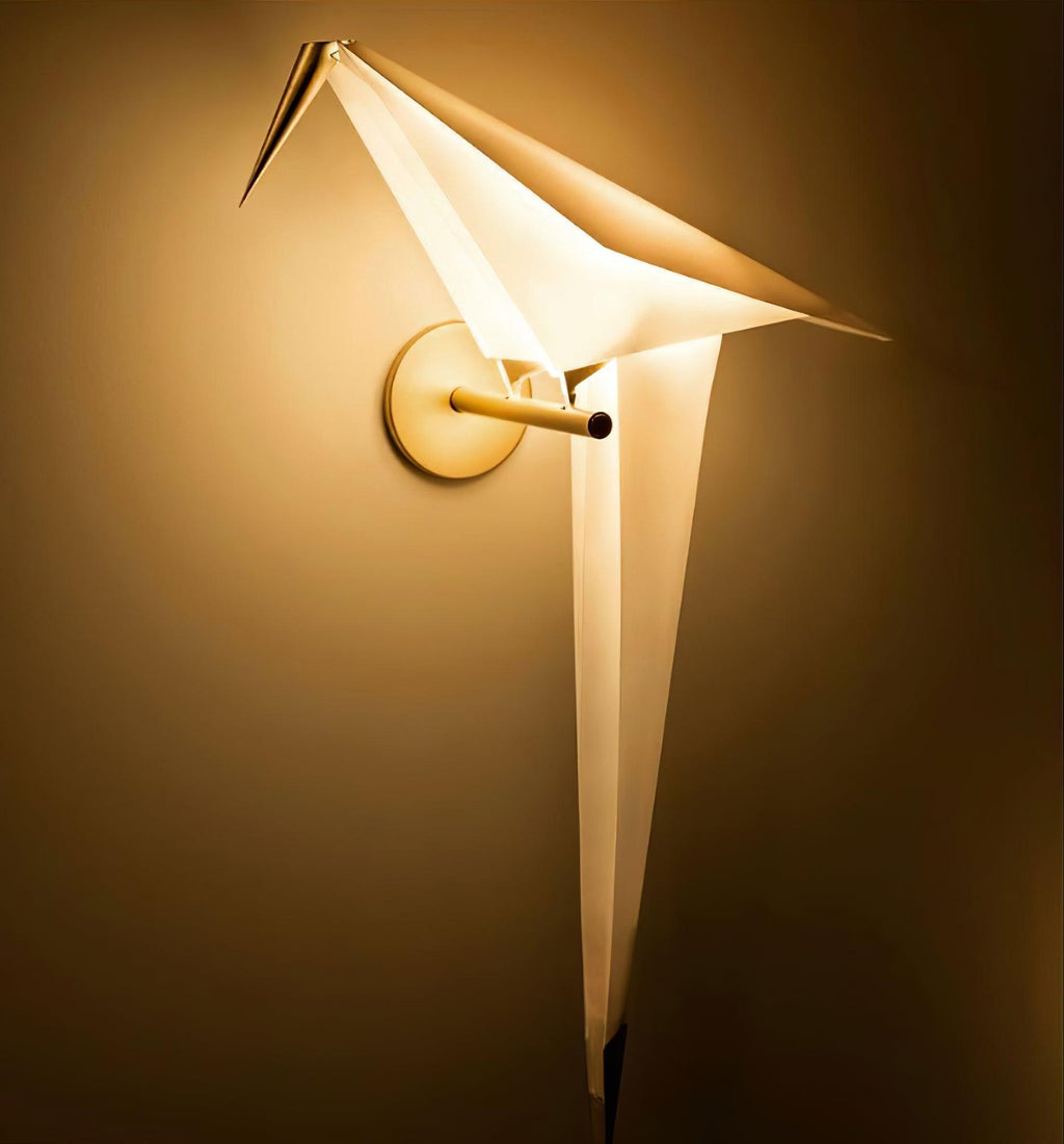 Close view of a lit Clérachic bird wall light, the warm glow filling its folded white wings and tail against a golden wall.