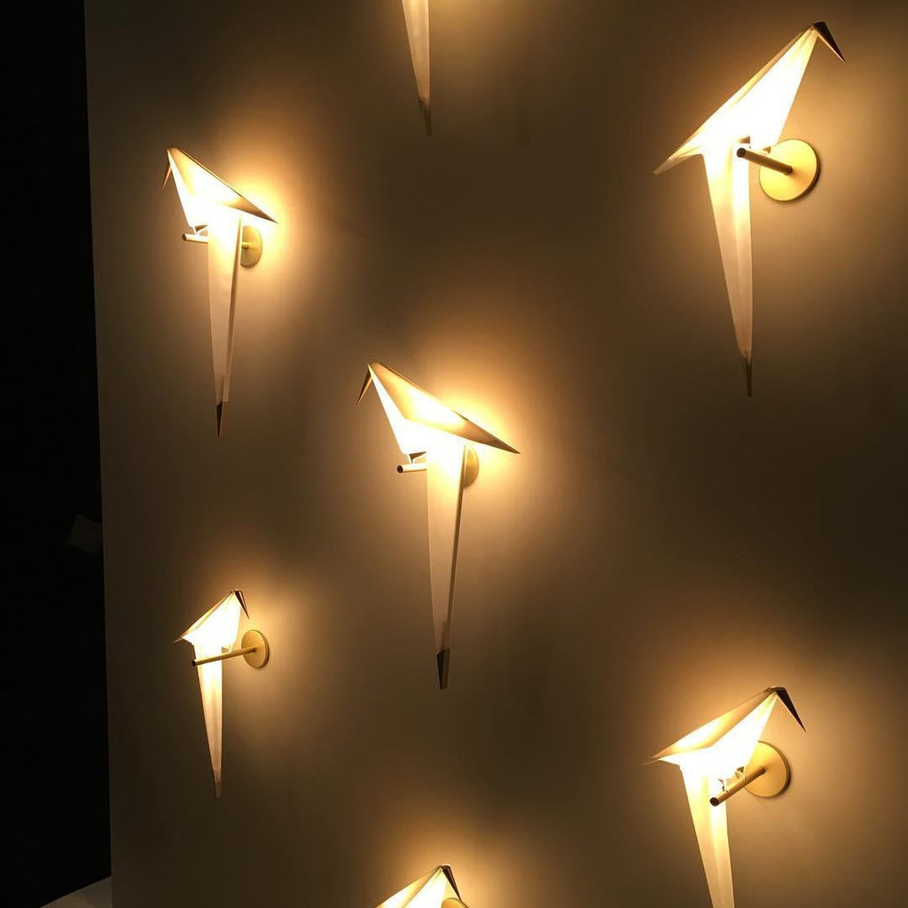 Five Clérachic bird wall lights glow at different angles on a dark wall, each casting a warm pool of light around it.
