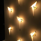 Five Clérachic bird wall lights glow at different angles on a dark wall, each casting a warm pool of light around it.
