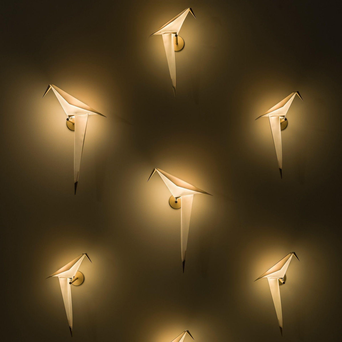 Six Clérachic bird wall lights glow on a dark wall, each lit warm and spaced out in a loose pattern.