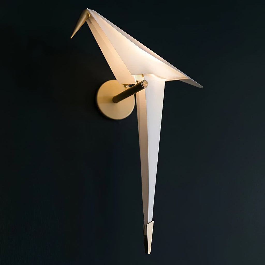 A Clérachic bird wall light, unlit, on a dark navy wall, its folded white wings and round gold backplate in sharp focus.