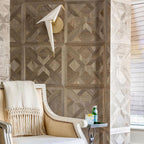 A Clérachic bird wall light, unlit, on a wall of patterned walnut-toned panels, next to a cream chair with a fringed throw.
