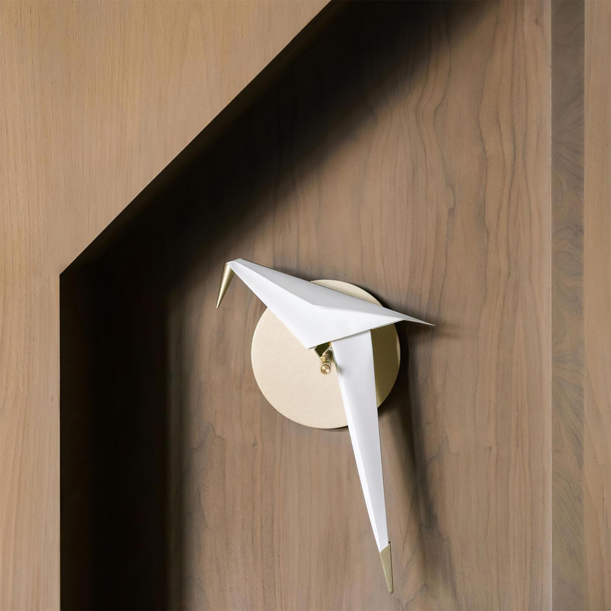 An unlit Clérachic bird wall light on a timber wall beside a deep shadowed recess, with a small round cream backplate.