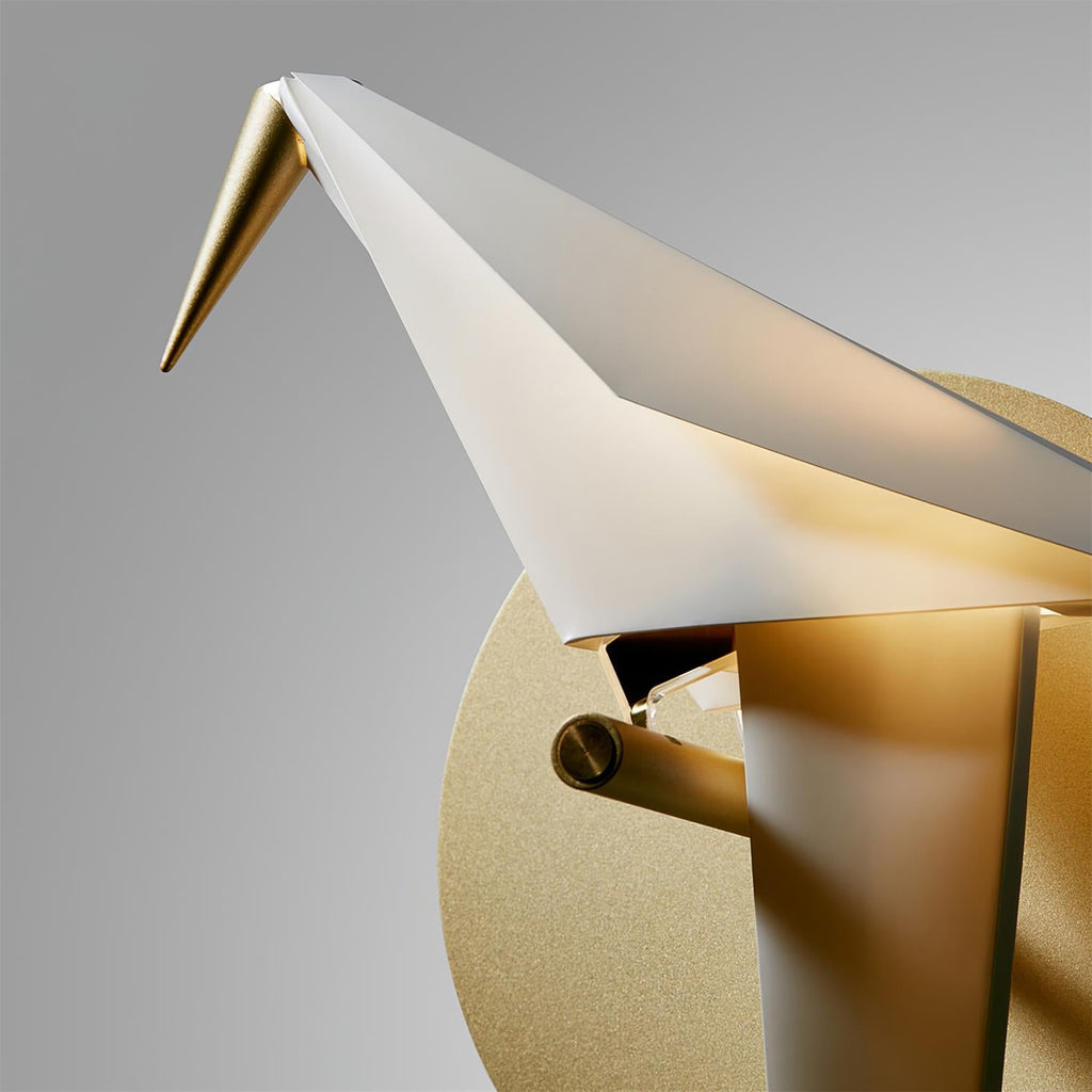 Close view of the head, folded wing and gold beak of this Clérachic bird wall light, with its gold perch and round backplate.