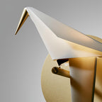 Close view of the head, folded wing and gold beak of this Clérachic bird wall light, with its gold perch and round backplate.