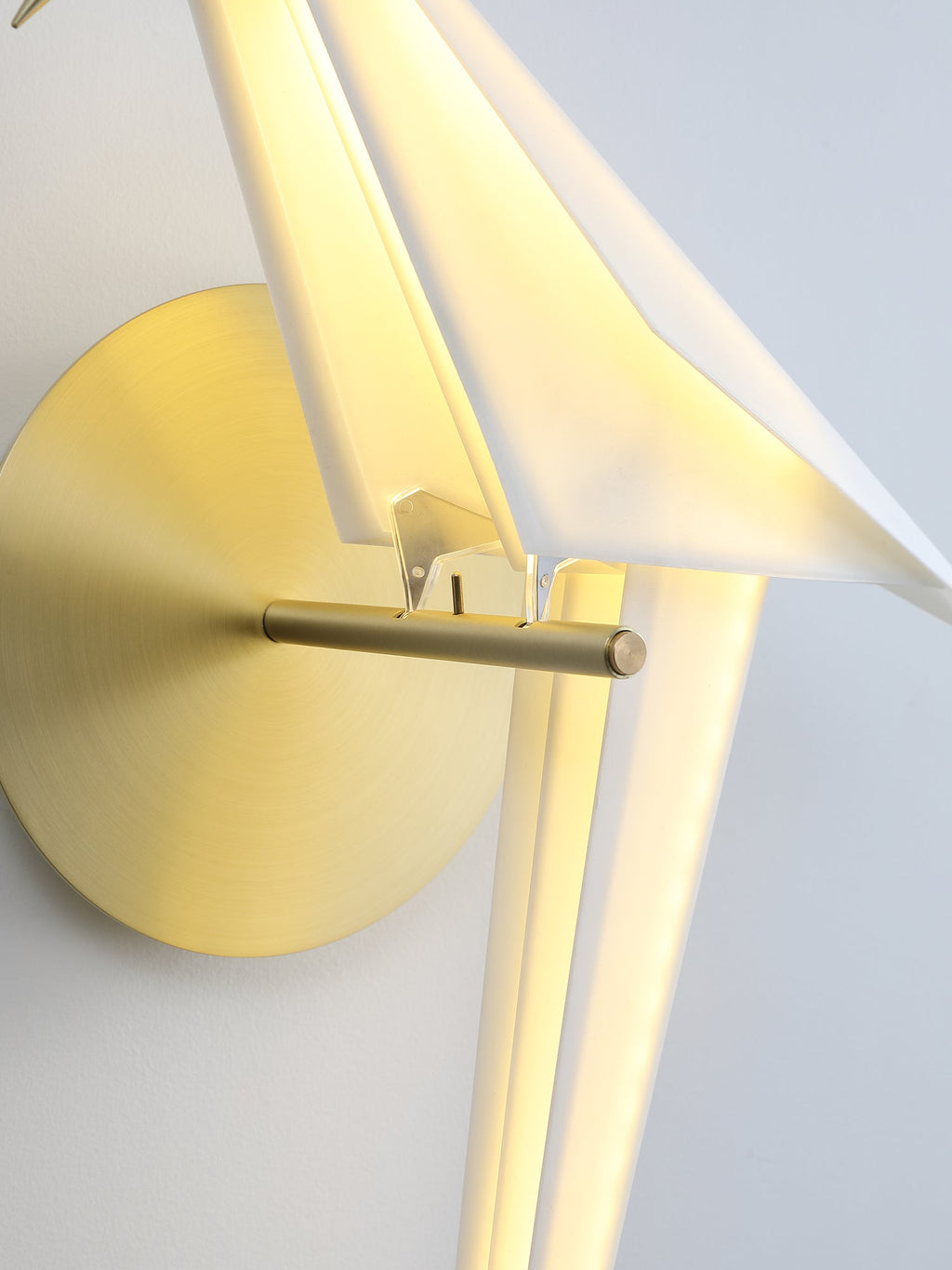 Close view of the gold perch and backplate on a Clérachic bird wall light, with the lit white body behind them.