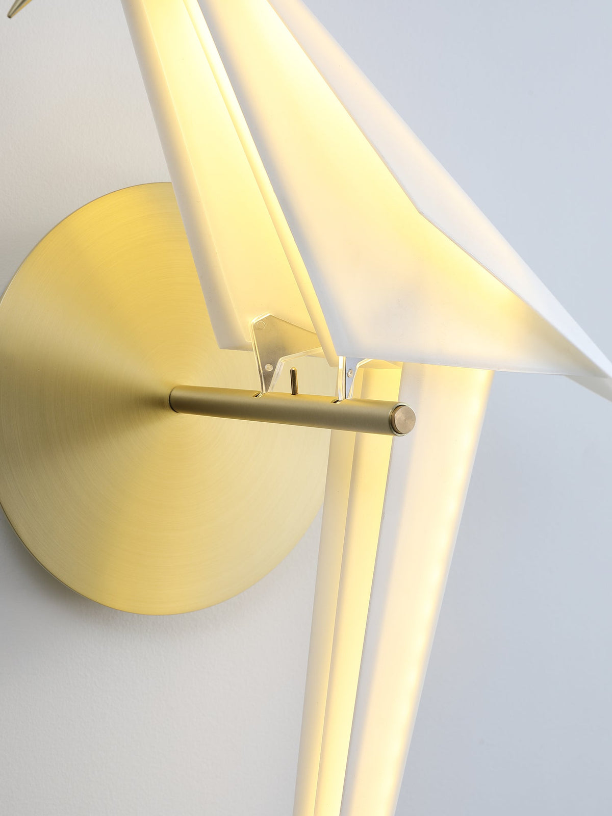 Close view of the gold perch and backplate on a Clérachic bird wall light, with the lit white body behind them.