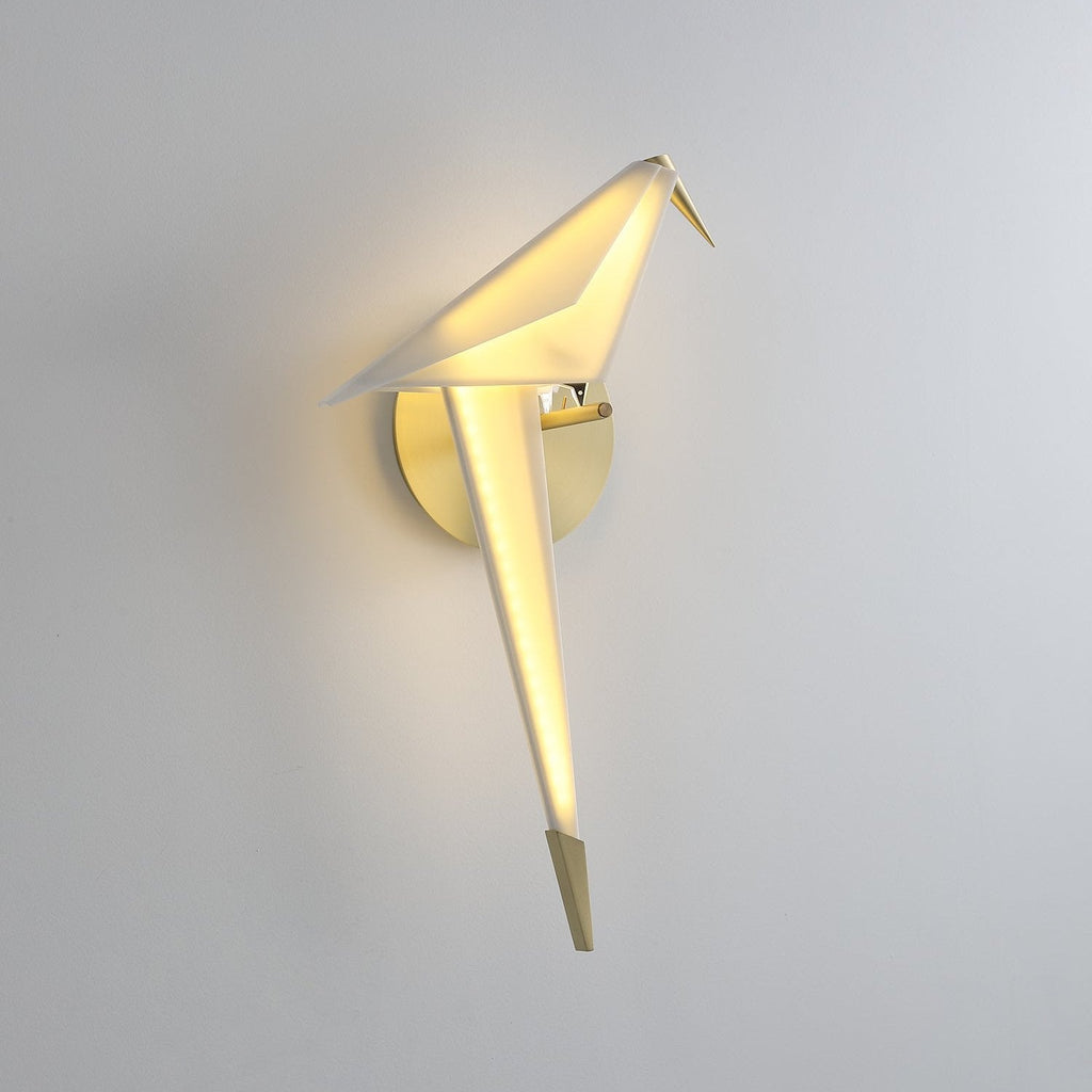Seen from the side, this lit Clérachic bird wall light glows from its white back and tail, with a gold beak on a pale wall.