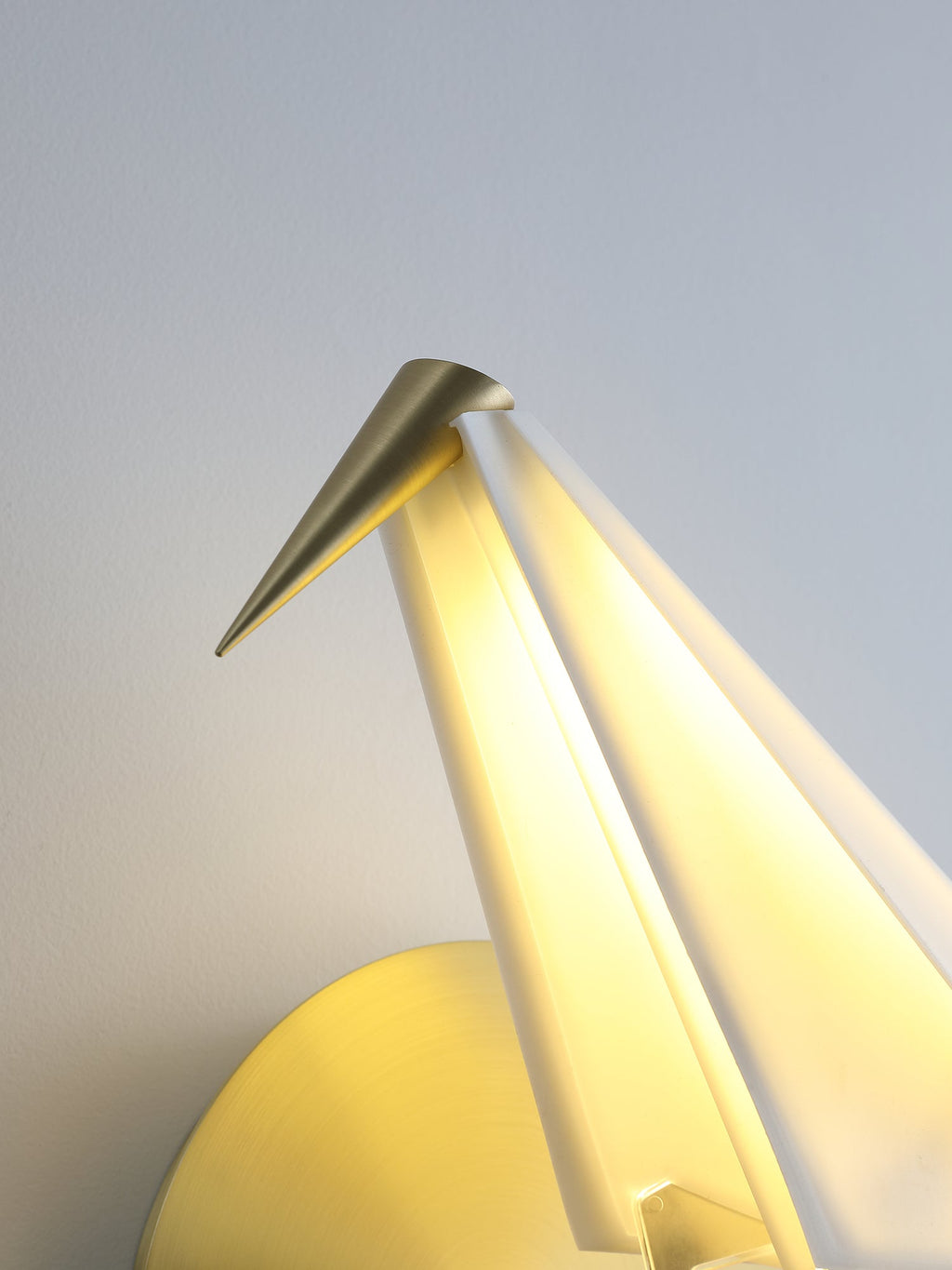 Close view of the gold beak and the glowing folded head of this Clérachic bird wall light, with the gold backplate behind it.