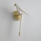 An unlit Clérachic bird wall light on a pale grey wall, its folded white body leaning forward on a gold perch.