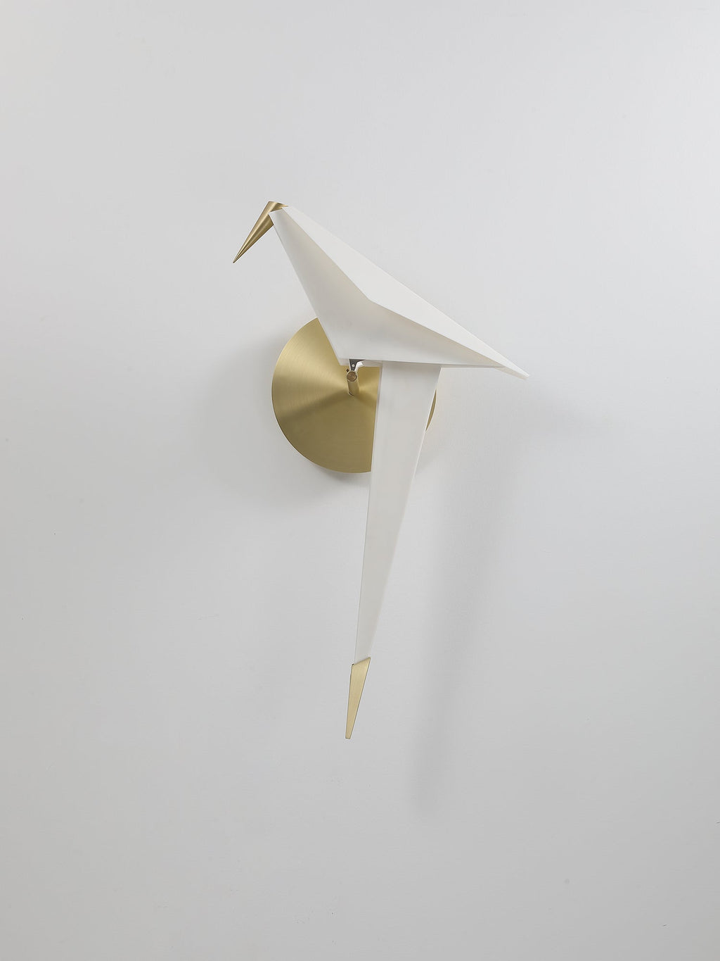 A smaller view of this unlit Clérachic bird wall light on a pale wall, with a brushed gold backplate and a gold tail tip.