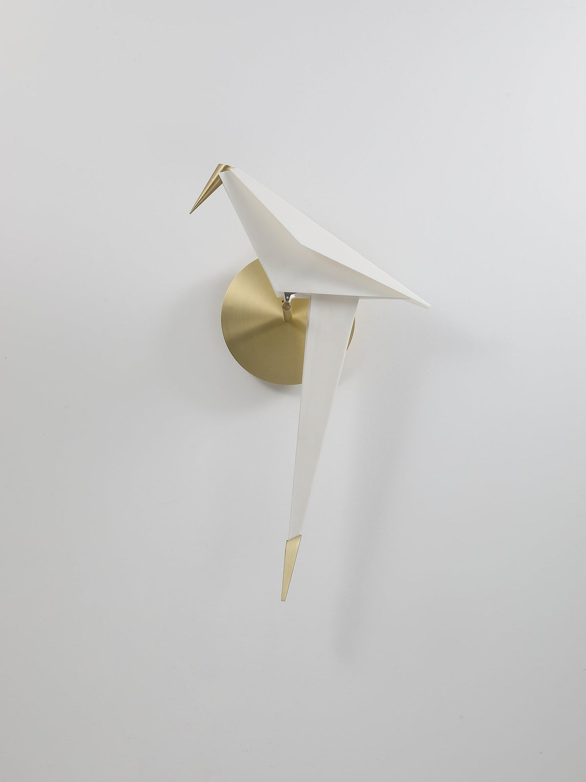 A smaller view of this unlit Clérachic bird wall light on a pale wall, with a brushed gold backplate and a gold tail tip.
