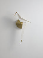 A Clérachic bird wall light, unlit, on a pale wall, shown small with its white folded body and brushed gold backplate.