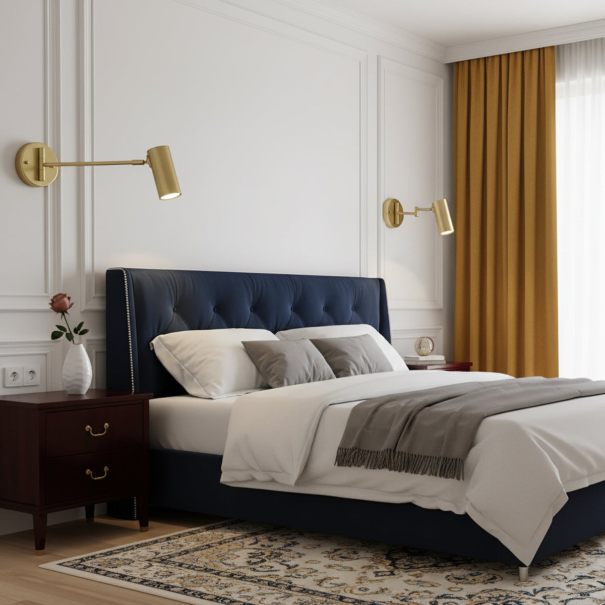 A pair of Clérachic gold wall lights either side of a navy tufted headboard, in a bedroom with mustard curtains.