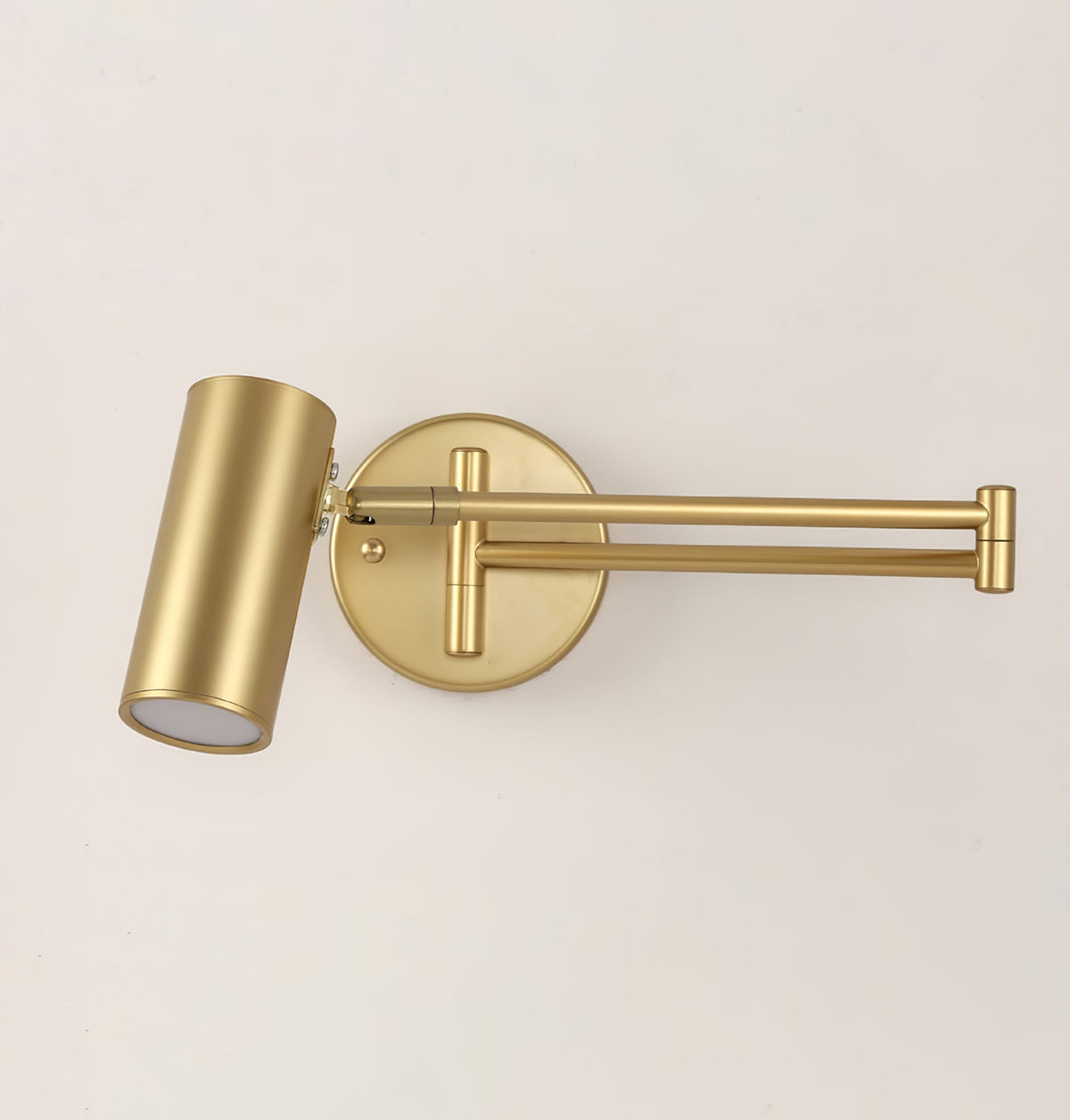Close view of a Clérachic gold wall light with a folded arm, its round backplate and the cylinder head with a frosted lens.
