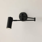 Clérachic wall light in black, with a round backplate, a folding arm and a cylinder head, on a pale wall.