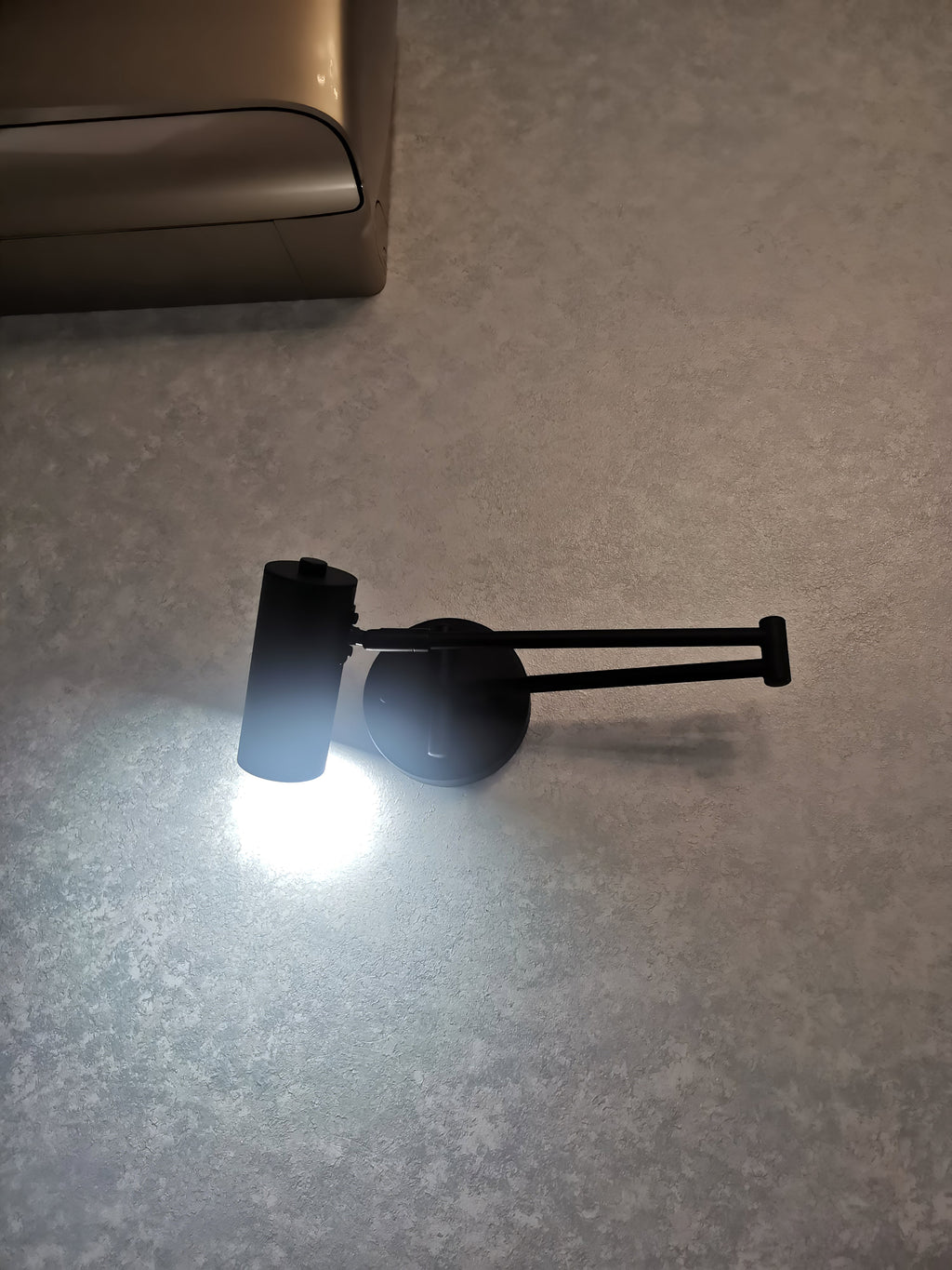 A Clérachic black wall light switched on, its head aimed down and giving off a bright white pool of light.