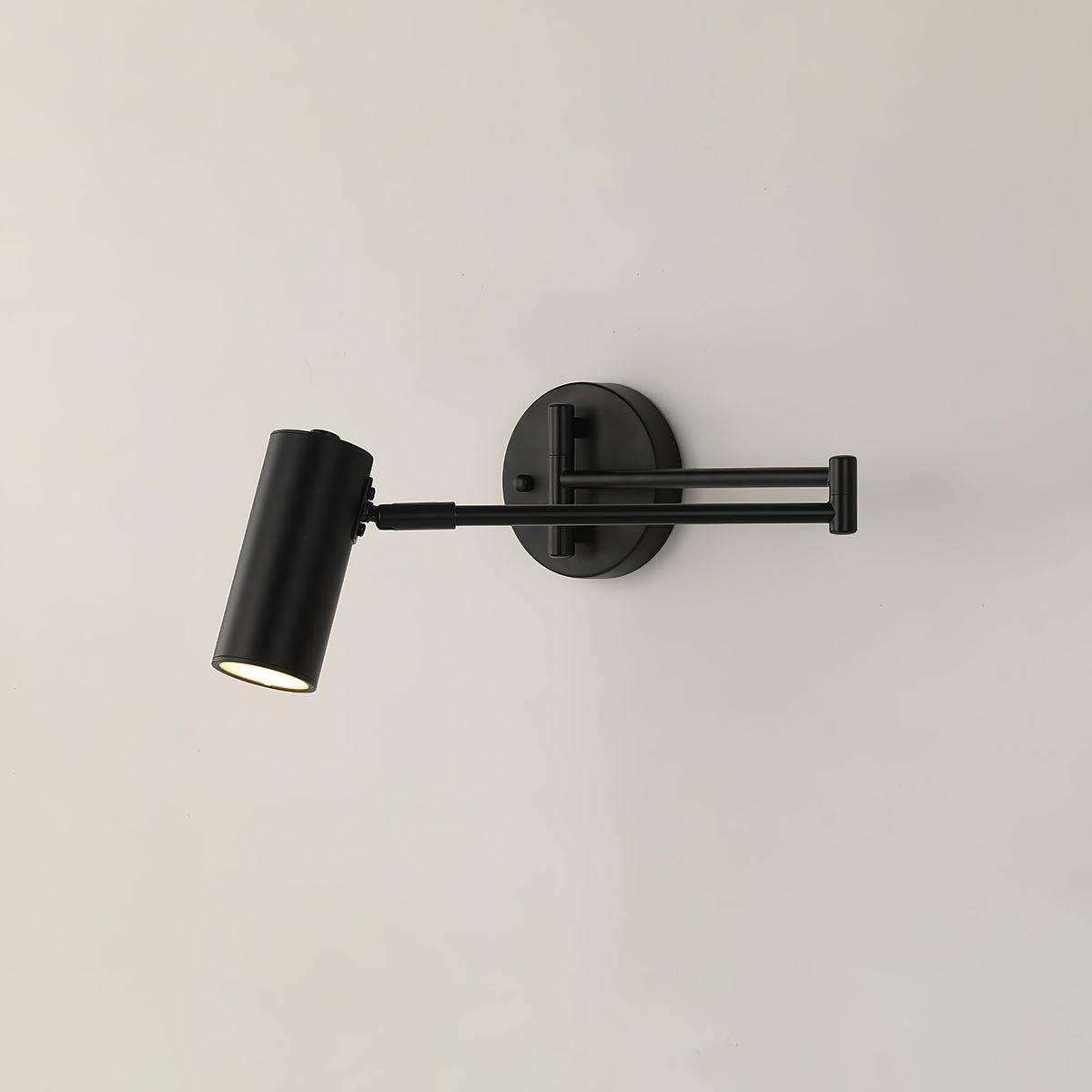 Clérachic wall light in black, with the arm folded and the cylinder head aimed down, on a plain pale wall.