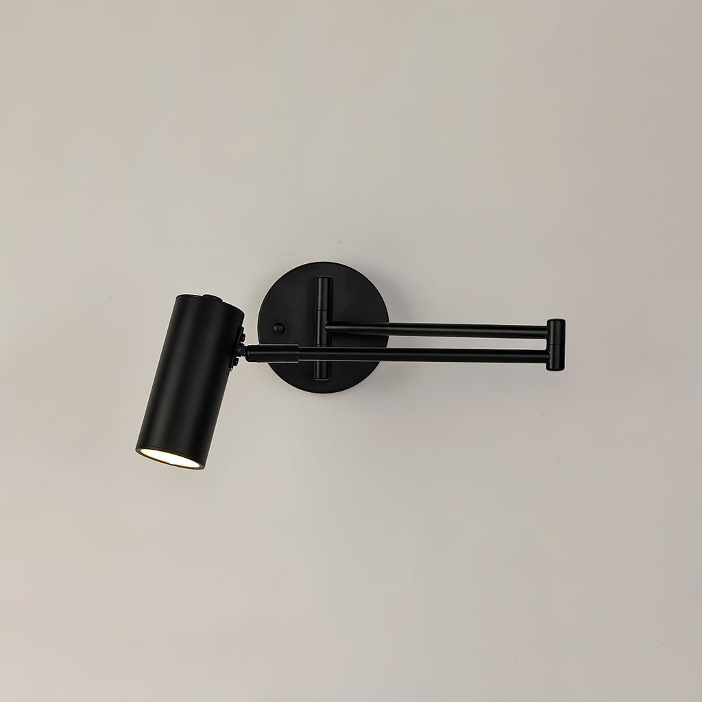 A black Clérachic wall light with a folded arm, a round backplate and a cylinder head on a cream wall.