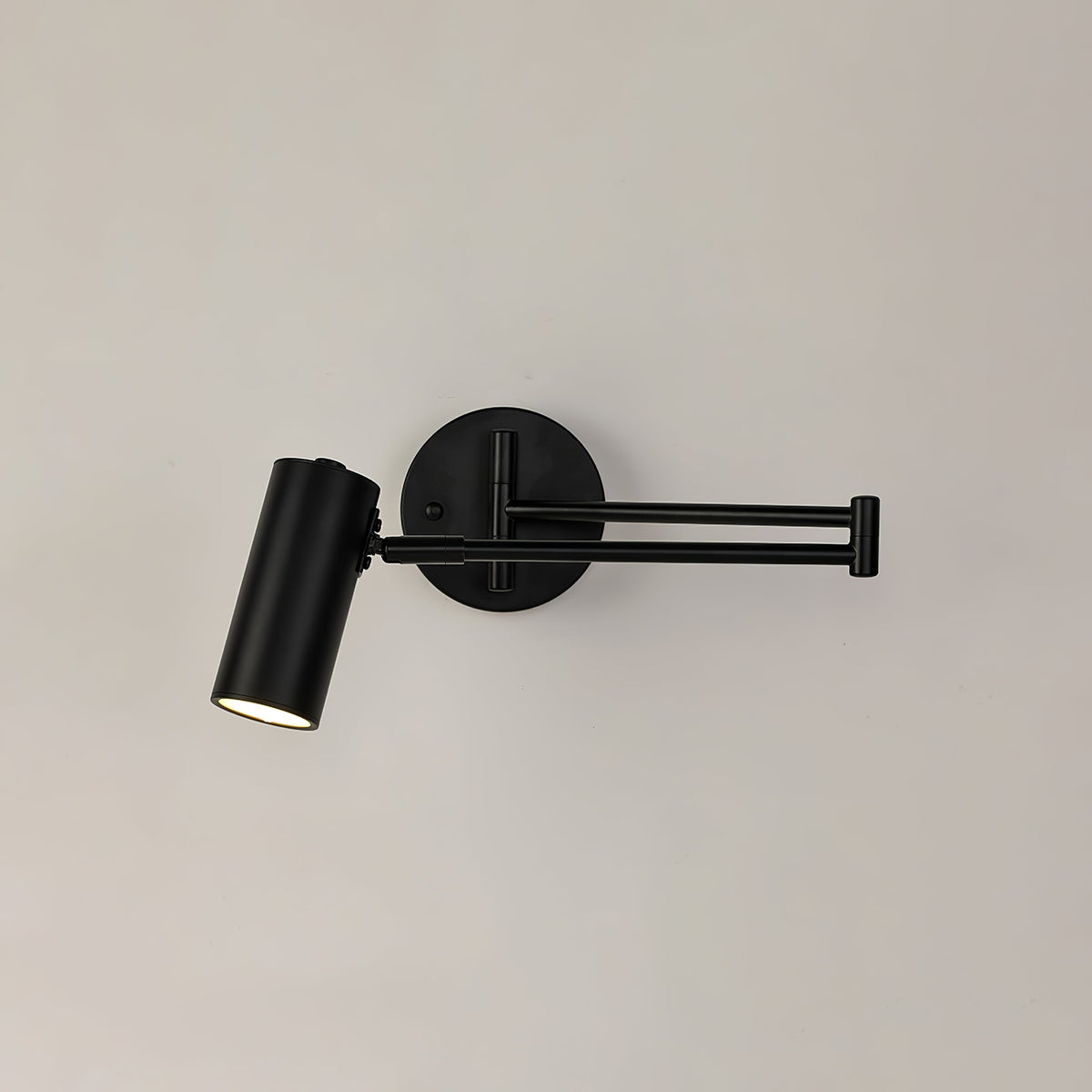 A black Clérachic wall light with a folded arm, a round backplate and a cylinder head on a cream wall.