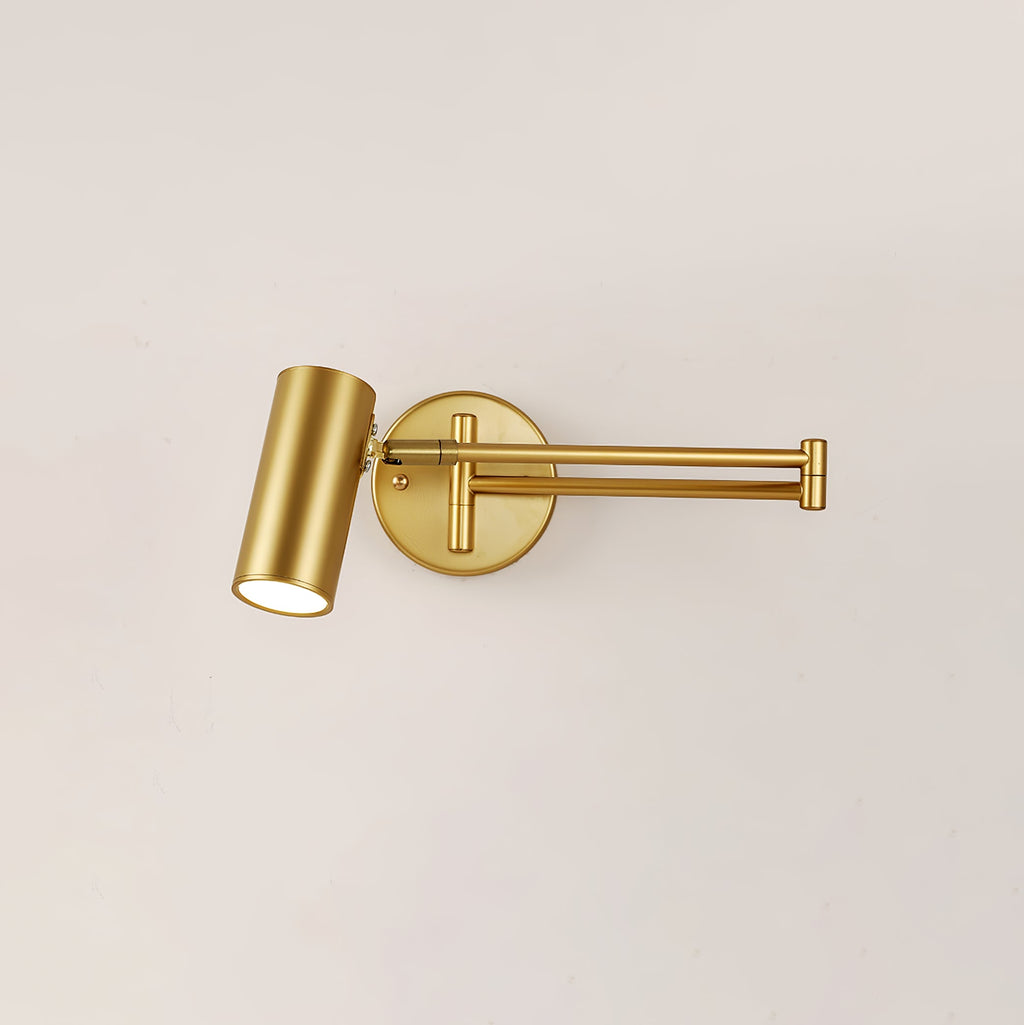 This Clérachic gold wall light with a long folding arm, on a cream wall, with the cylinder head tilted down.