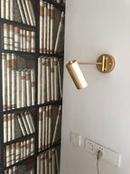 Clérachic gold wall light mounted beside a bookcase-patterned panel, above a power socket strip.
