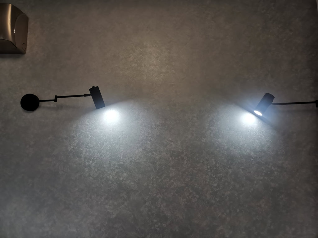 Two Clérachic black wall lights switched on at night, each shining a cool white beam down a dark wall.