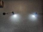 Two Clérachic black wall lights switched on at night, each shining a cool white beam down a dark wall.