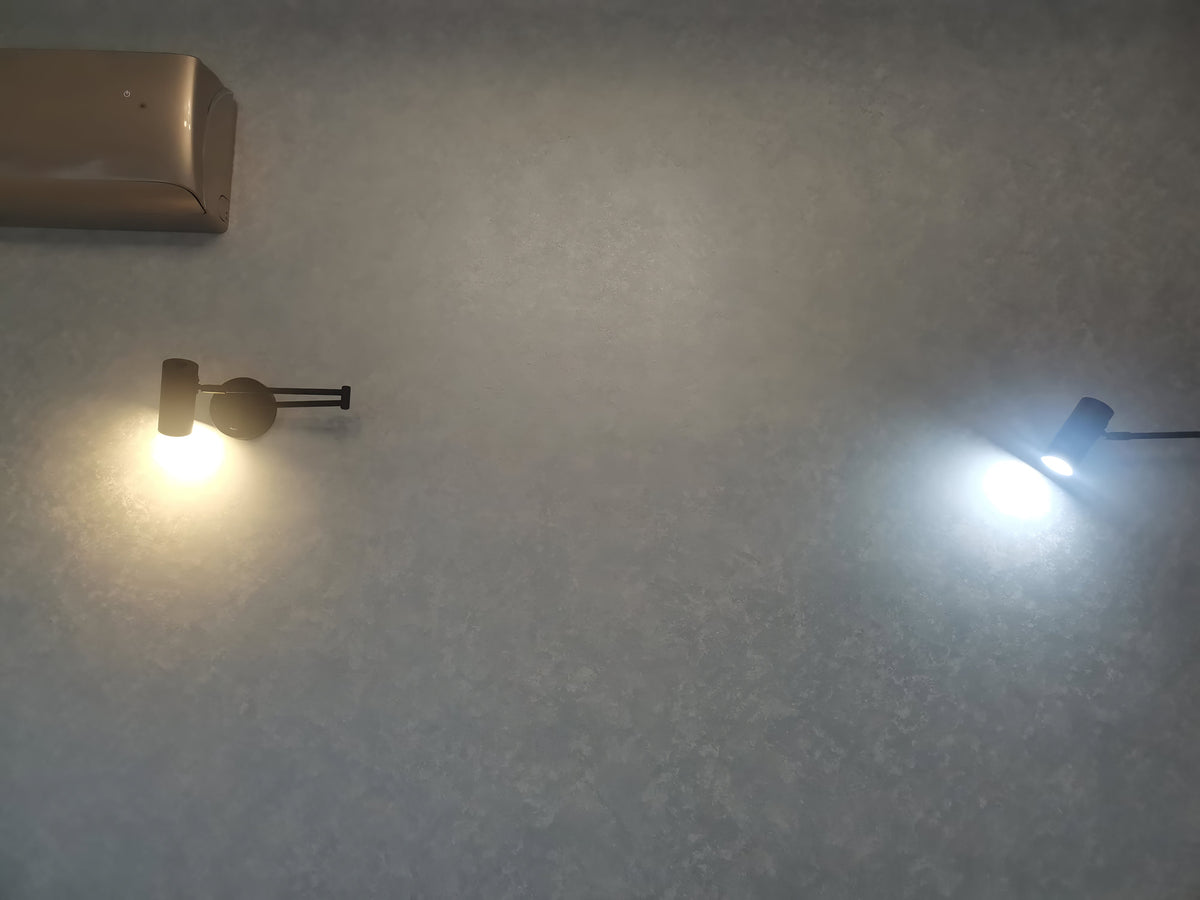 Two Clérachic wall lights on a dark wall, one giving a warm glow and one a cool white light.