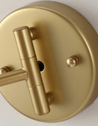 Close view of the round gold backplate on this Clérachic wall light, with the pivot joint and two small knurled screws.
