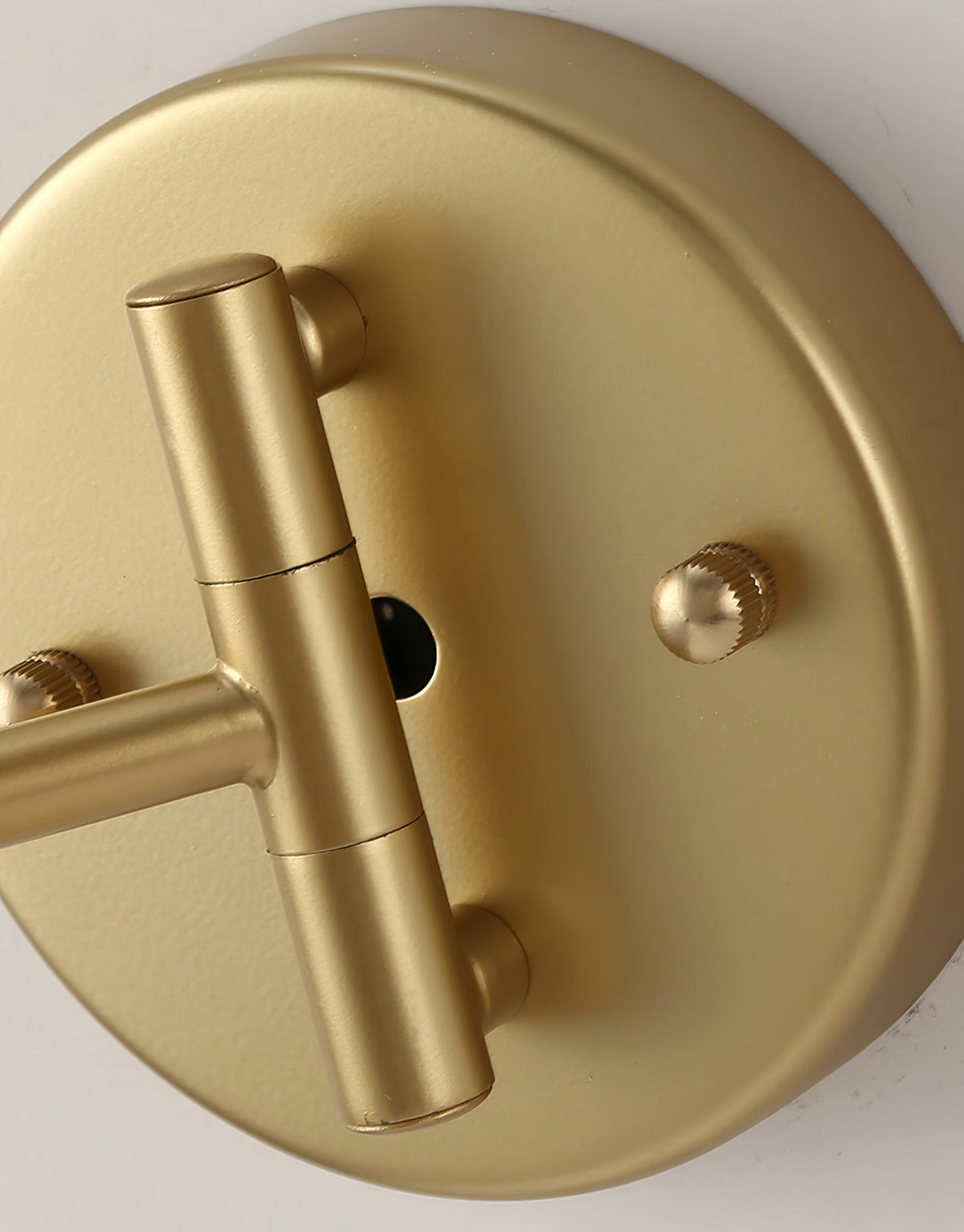 Close view of the round gold backplate on this Clérachic wall light, with the pivot joint and two small knurled screws.