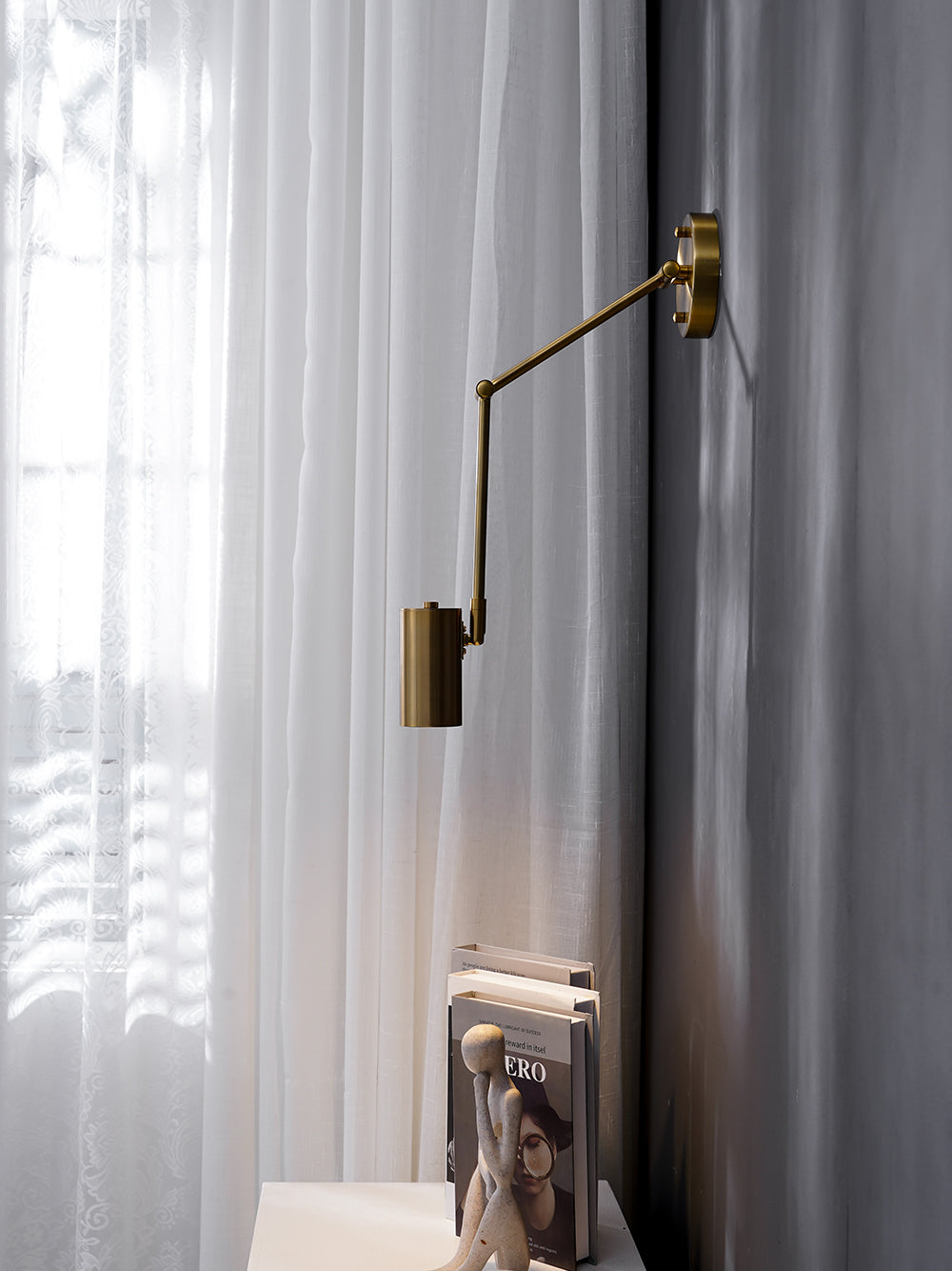 The Clérachic gold wall light seen from a different angle, its arm swung out and its head hanging beside curtains.