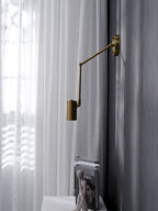 Clérachic gold wall light with its drop arm, hanging above a white console, a stack of books and a sheer curtain.