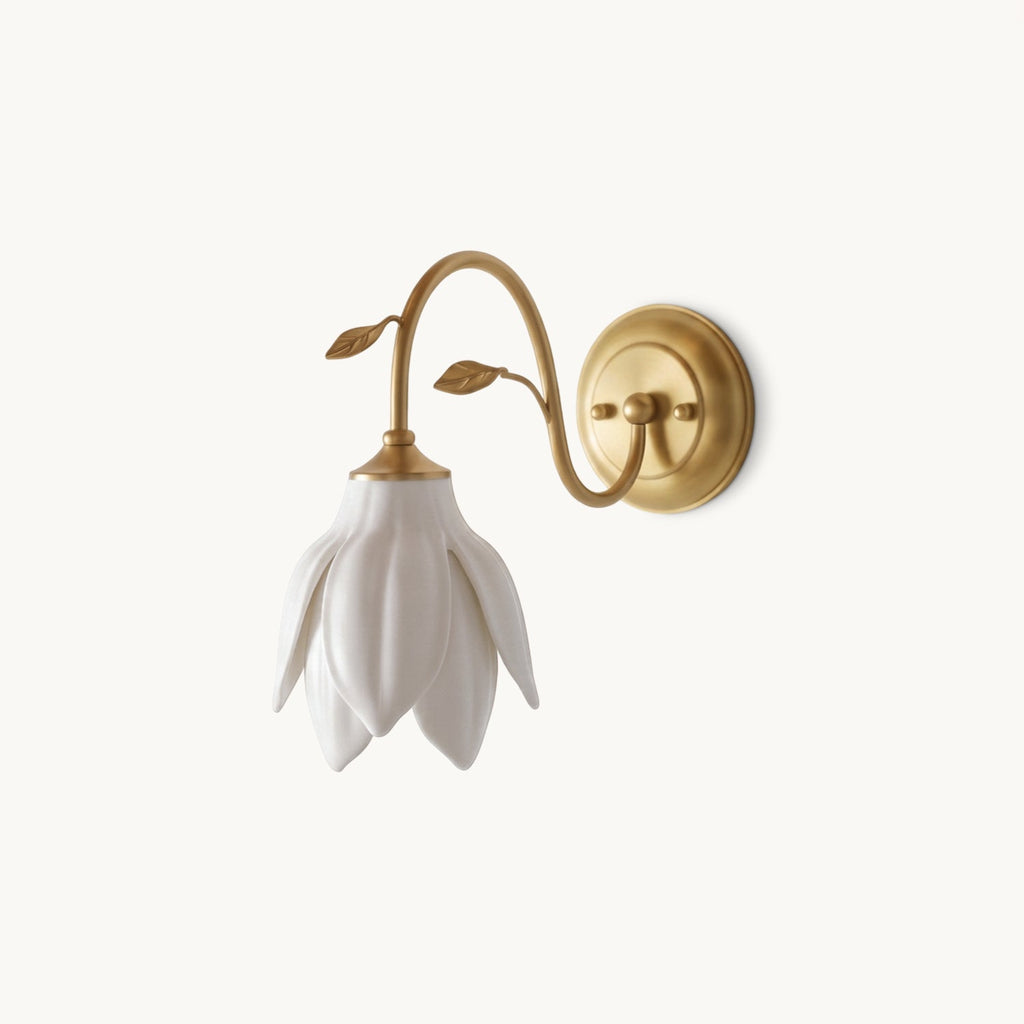 White ceramic petal shade hanging down from a curved gold arm with two small leaves, this Clérachic wall light on a plain white backdrop.