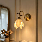 Lit petal shade on a curved gold arm, this Clérachic wall light glowing warmly on a panelled wall above a vase of dried roses.