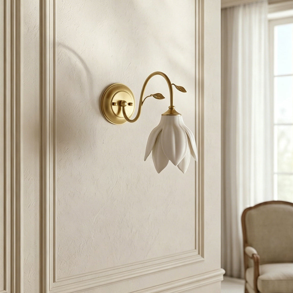 Unlit white petal shade hanging from a gold arm on a panelled cream wall, this Clérachic wall light with a chair edge and window at the side.