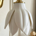 Close view of the glossy white ceramic petals and the gold collar at the top of the shade on this Clérachic wall light.