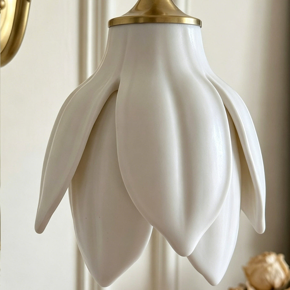 Close view of the glossy white ceramic petals and the gold collar at the top of the shade on this Clérachic wall light.