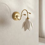 Clérachic wall light with a downward petal shade and curved gold arm on a textured cream wall, with a window frame at the right.