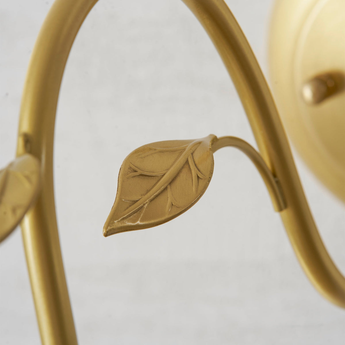Close view of a single gold leaf on the curved arm of this Clérachic wall light, with the round wall plate blurred behind.
