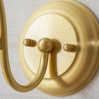 Close view of the brushed gold round wall plate with its two screw caps and the arm base of this Clérachic wall light.