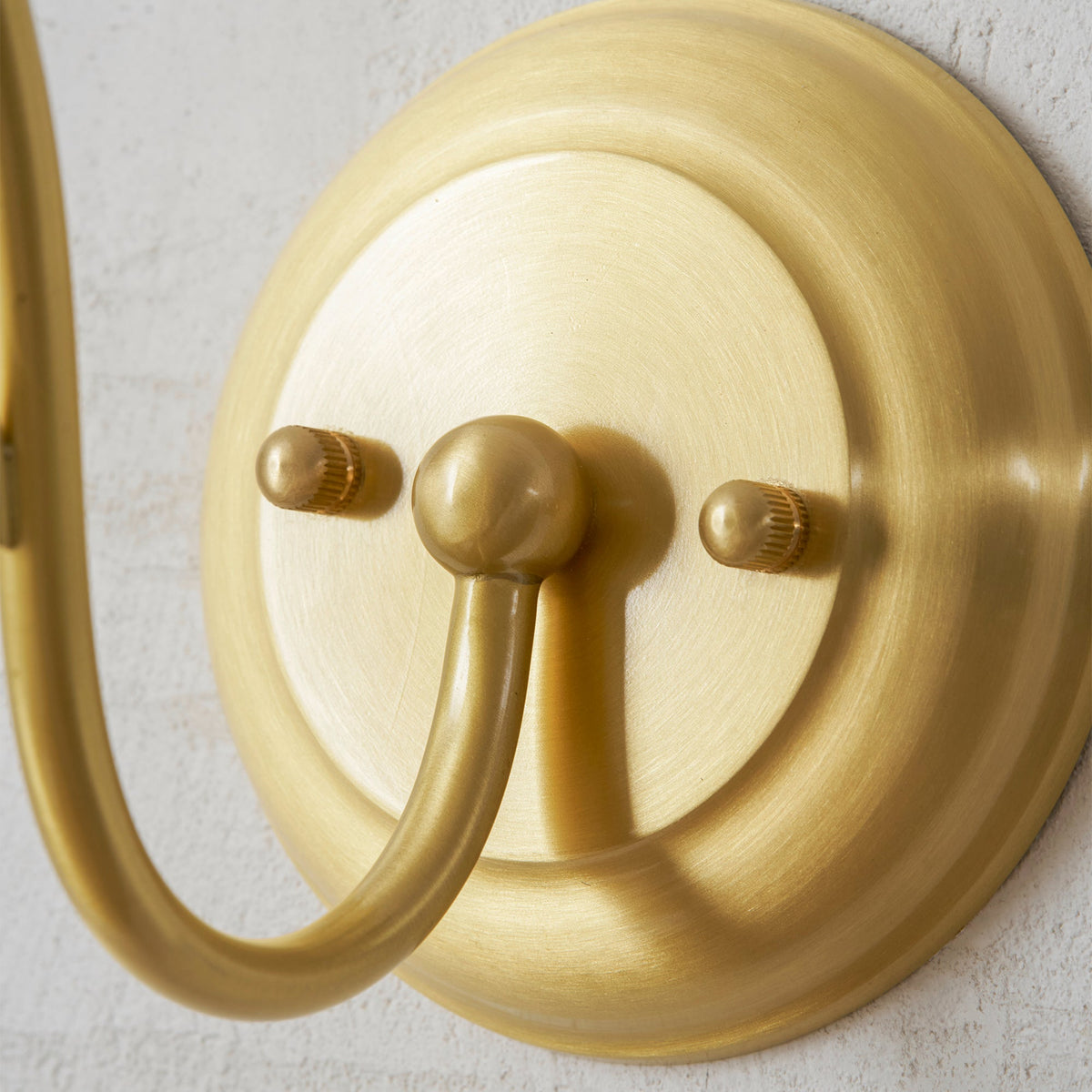 Close view of the brushed gold round wall plate with its two screw caps and the arm base of this Clérachic wall light.