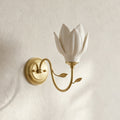 Upward-facing white petal shade on a curved gold arm, this Clérachic wall light shown on a textured cream plaster wall.