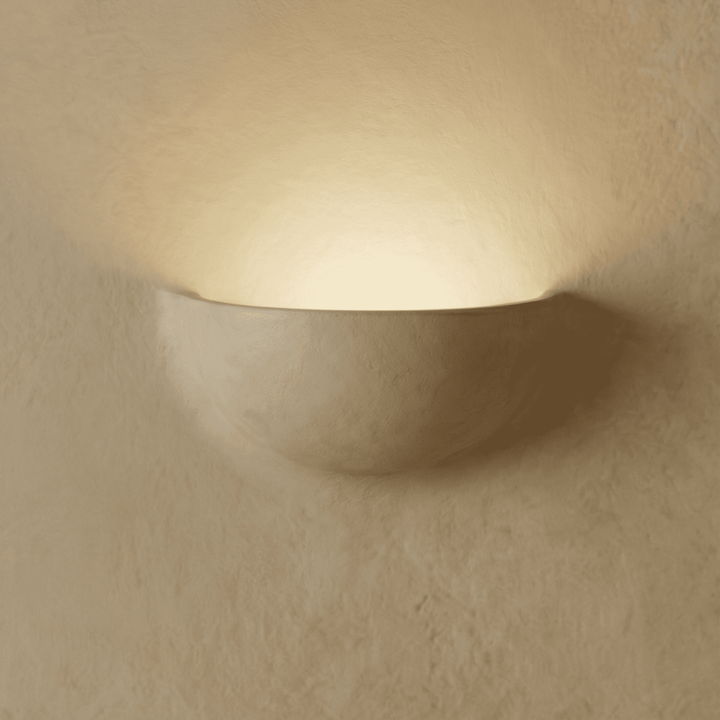 Clérachic half-moon plaster wall light glowing upward on a limewashed wall, its matte white shell casting a warm halo.